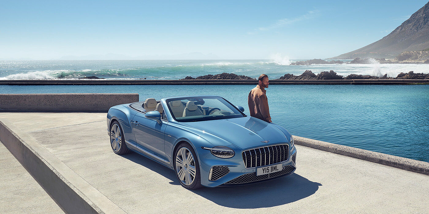 Bentley Guatemala New Bentley Continental GTC Azure convertible front view in Light Windsor blue paint with 22 inch ten spoke wheels parked by the sea in the sunshine