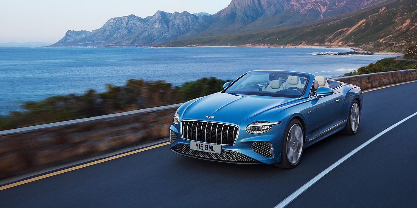 Bentley Guatemala New Bentley Continental GTC Azure convertible in Light Windsor blue paint with 22 inch Azure wheels and chrome grill, driving dynamically by the sea