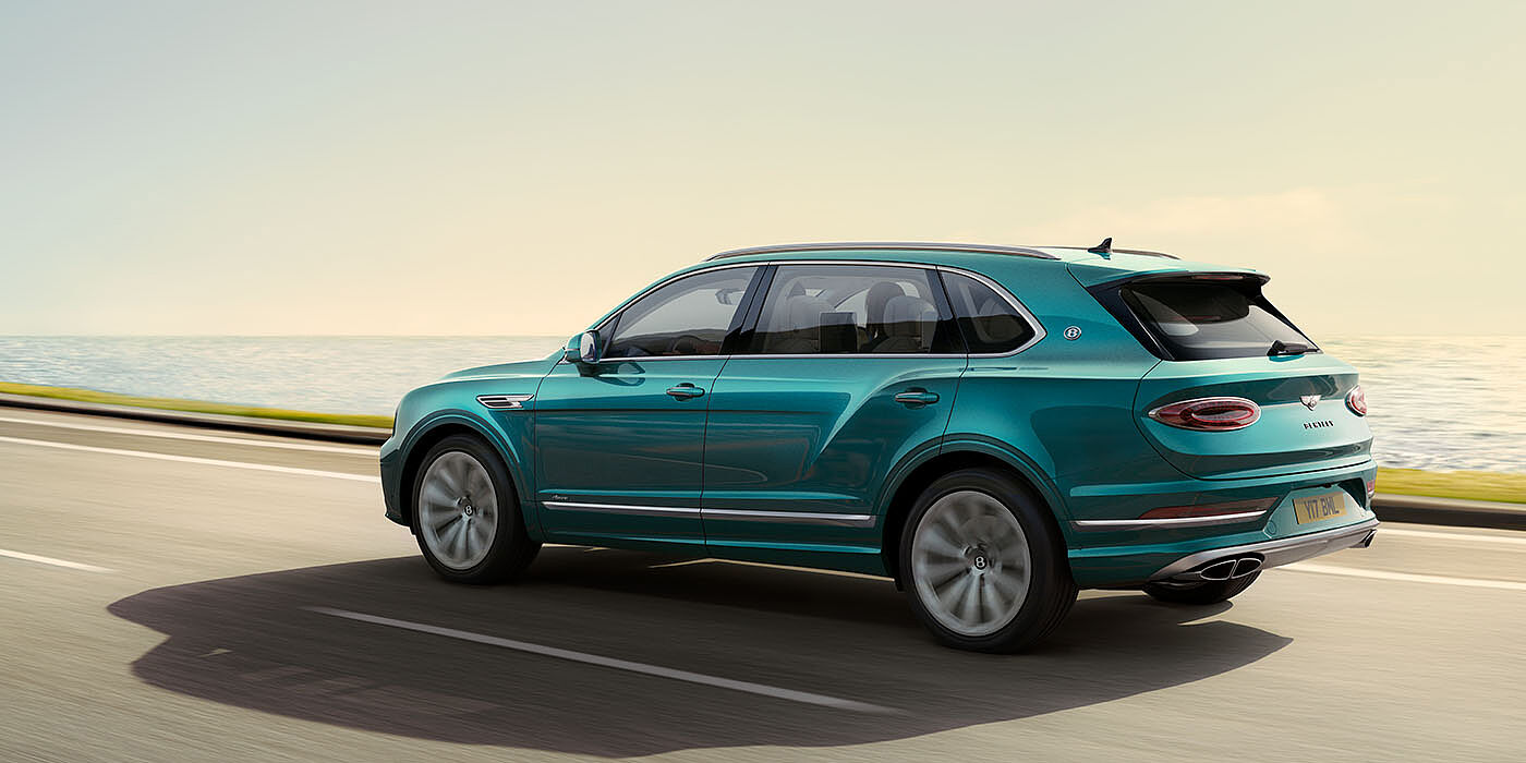 Bentley Guatemala Bentley Bentayga Extended Wheelbase Azure luxury SUV rear three quarter in Topaz Blue by Mulliner paint, driving on an ocean road.
