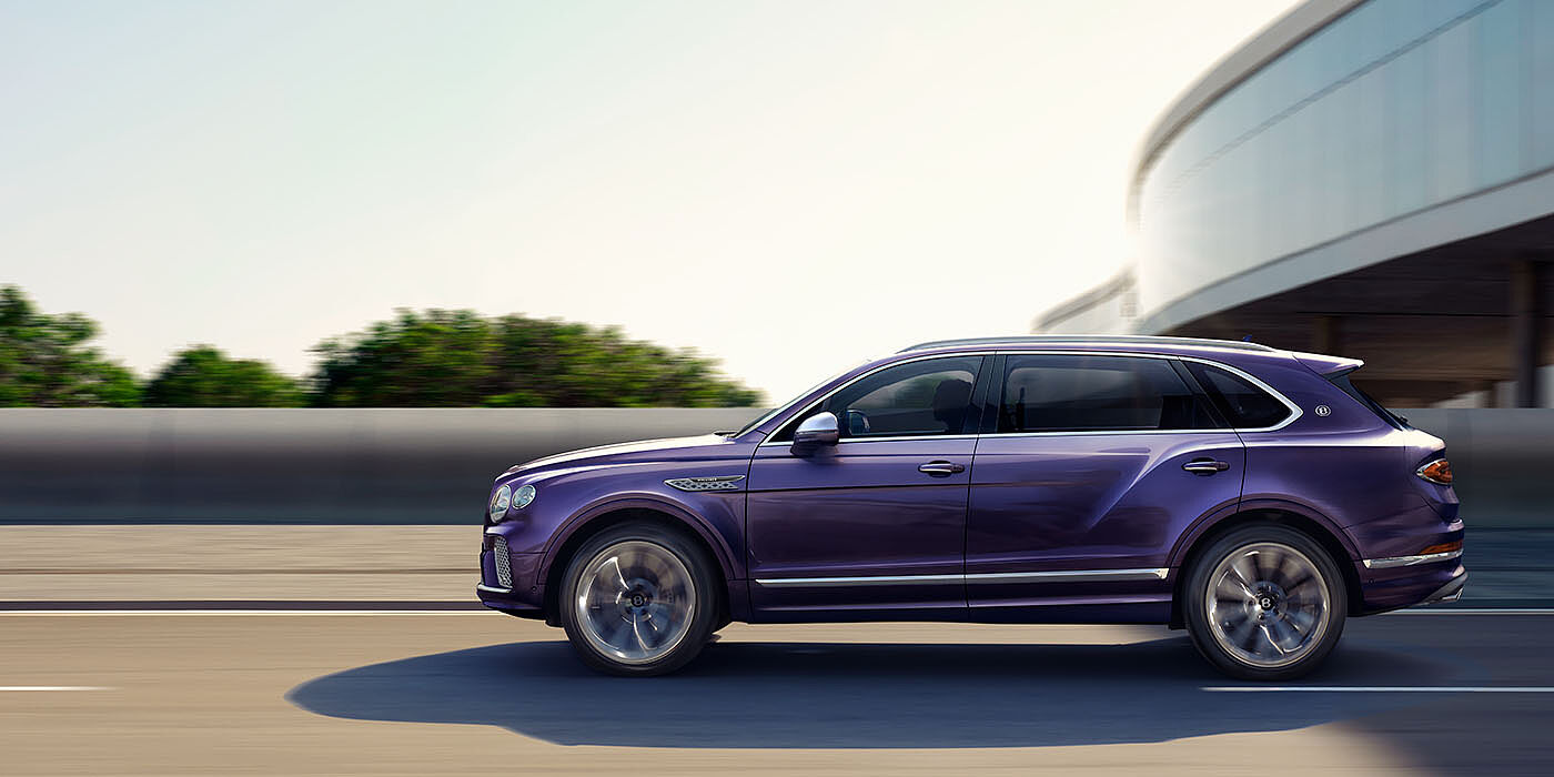 Bentley Guatemala Bentley Bentayga Extended Wheelbase Mulliner luxury SUV profile in Tanzanite Purple paint, driving on an country road past trees.
