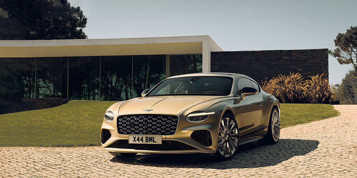 Bentley Guatemala Bentley Continental GT Mulliner coupe front three quarters in Patina paint parked outside a glass fronted building with a grass lawn behind it