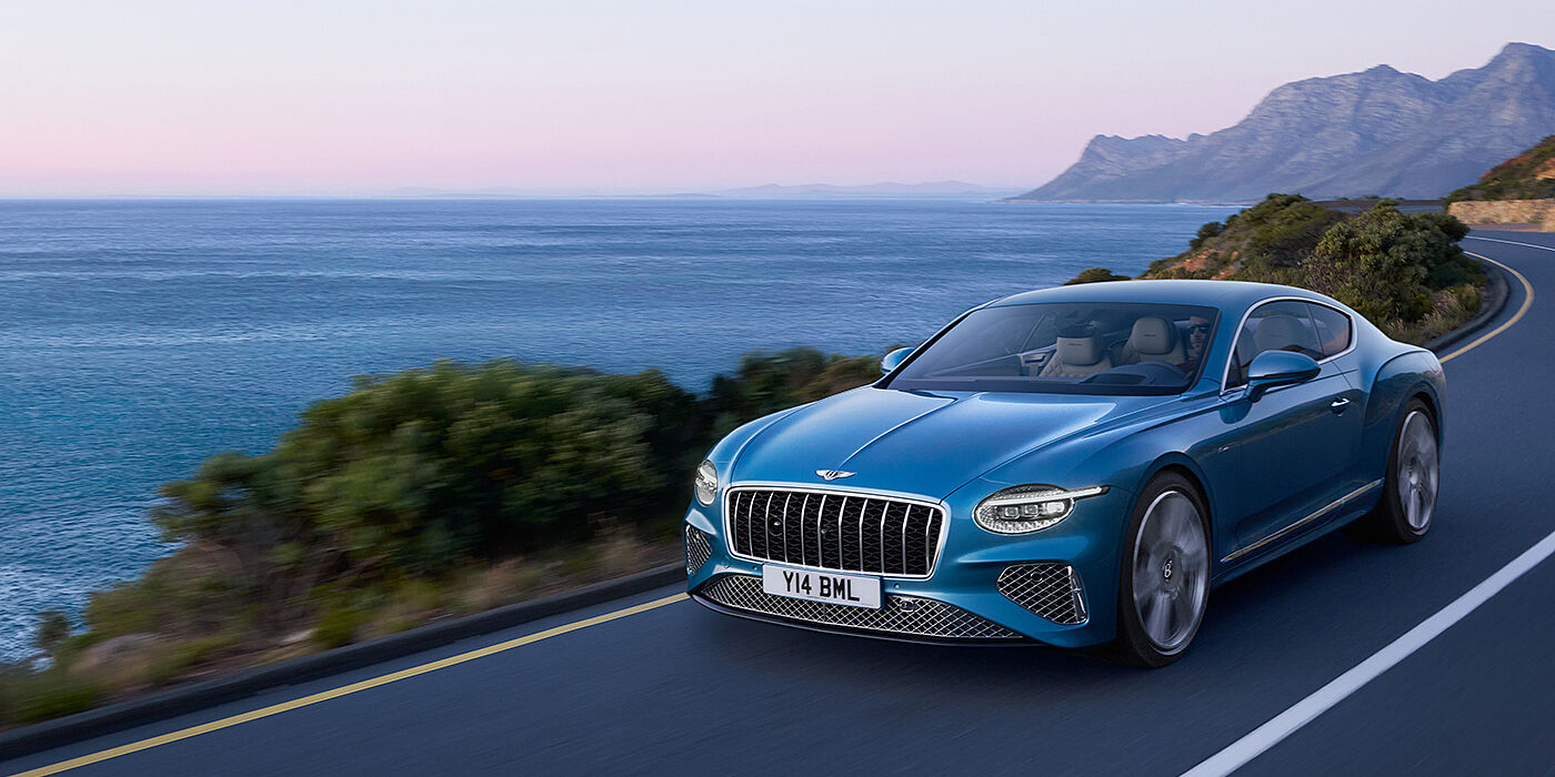 Bentley Guatemala New Bentley Continental GT Azure coupe in Light Windsor blue paint with 22 inch Azure wheels and chrome grill, driving dynamically by the sea