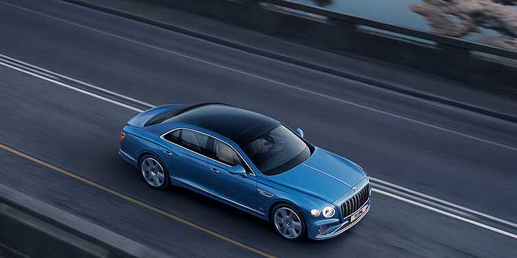 Bentley Guatemala New Bentley Flying Spur Azure sedan in Light windsor blue paint by Mulliner, with 22 inch Azure wheels seen from overhead driving dynamically on a country road