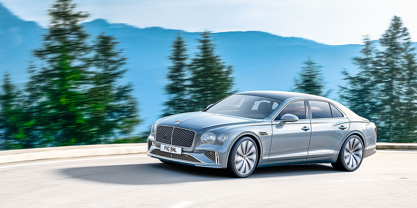 Bentley Guatemala New Bentley Flying Spur sedan side view in Silverlake paint with ten spoke wheels and chrome matrix grille driving dynamically on a mountain road