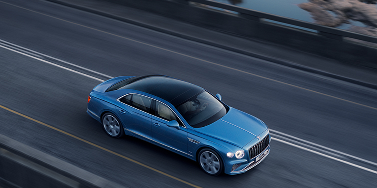 Bentley Guatemala New Bentley Flying Spur Azure sedan in Light windsor blue paint by Mulliner, with 22 inch Azure wheels seen from overhead driving dynamically on a country road
