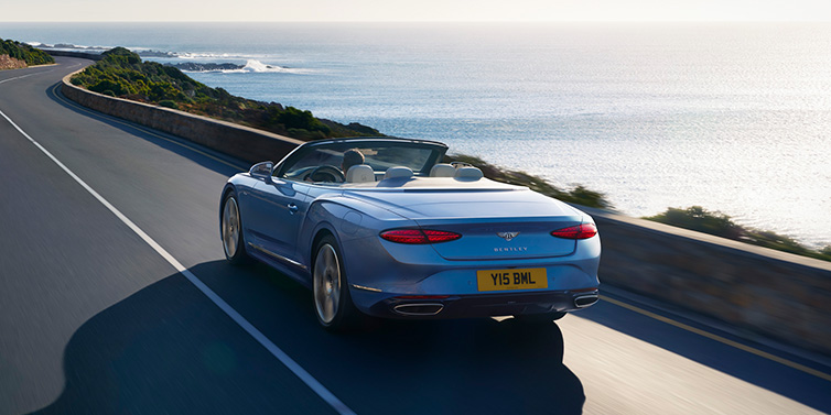 Bentley Guatemala New Bentley Continental GTC Azure convertible rear view in Light Windsor blue paint with 22 inch ten spoke wheels driving dynamically on an ocean road in the sunshine