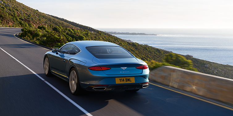 Bentley Guatemala New Bentley Continental GT Azure coupe in Light Windsor blue paint seen from the rear driving dynamically on a seaside road